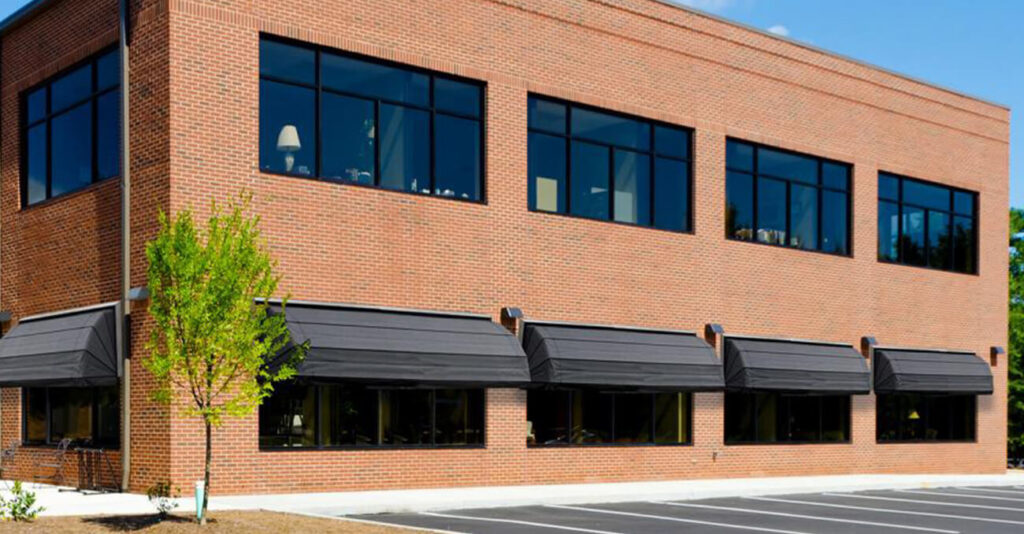 Korbmarkisen an einem modernen Gebäude mit großen Fenstern und Ziegelwand.