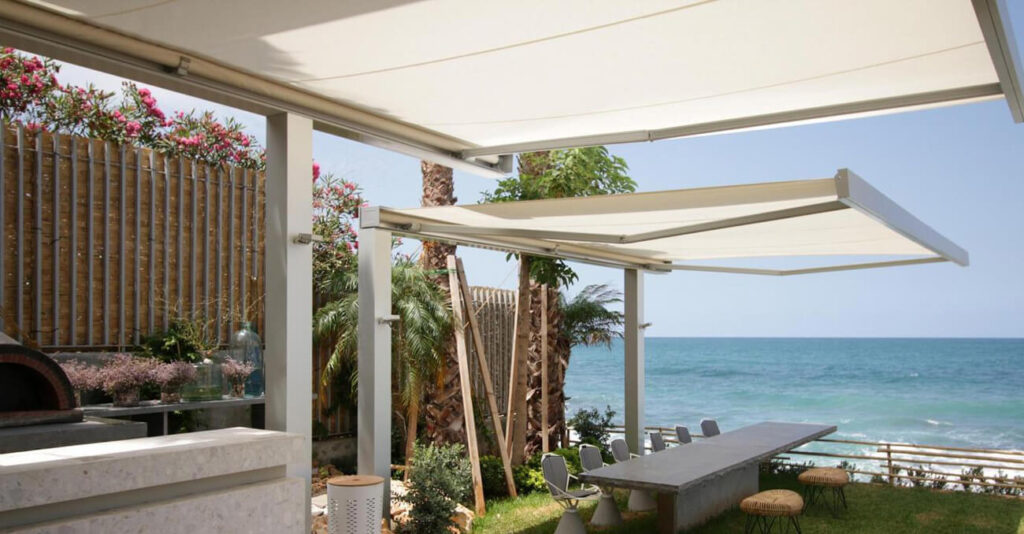 Eine große Markise, die über einem Tisch im Freien mit Blick auf das Meer gespannt ist.