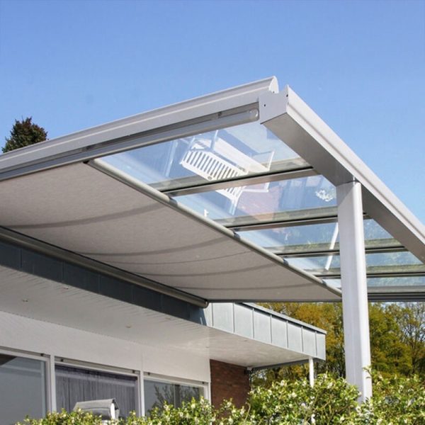 Modernes Glas-Terrassendach mit Metallrahmen, das aus einem Gebäude herausragt, von unten betrachtet. Die Struktur steht vor einem klaren blauen Himmel, an dessen Unterseite Grün zu sehen ist.